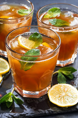 iced tea with mint and lemon in glasses on dark background, closeup vertical
