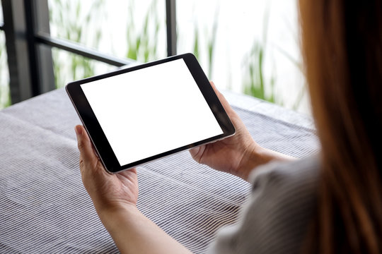 Mockup image of a woman holding black tablet pc with blank white desktop screen on table in cafe