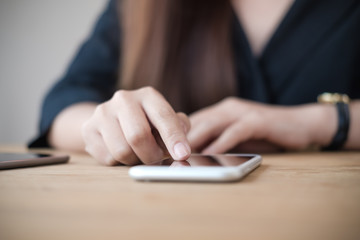 Fototapeta premium Closeup image of a woman using and touching smart phone on wooden table