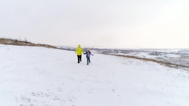 Mother and daughter holding hands and running together on snowfield. Aerial top shot