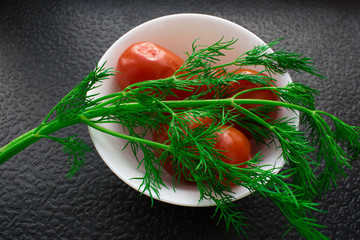 Marinated tomatoes on the home in a white round dish with a branch of fresh dill