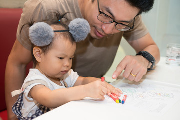 Little baby cute girl painting with crayon with father.