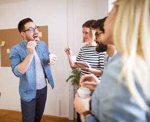Group of young playful happy coworkers having fun on break while together drinks coffee in the paper cup.
