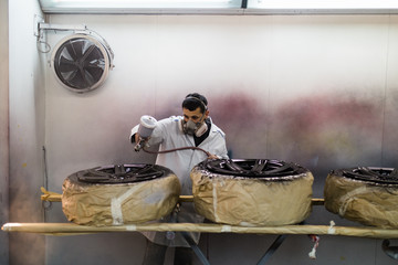 Man with protective clothes and mask painting car parts using spray compressor. Selective focus.