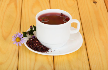 Cup of hot tea, crushed fruits of dry dog-rose on saucer, against background of table