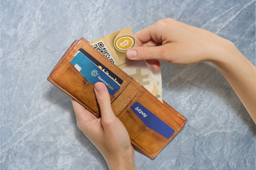 Portafoglio aperto con bitcoin cartacei e carte di credito virtuali, sfondo pietra