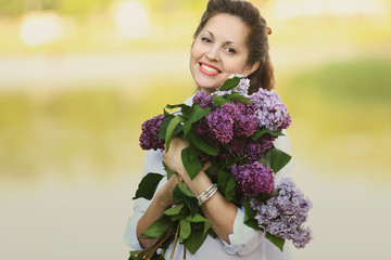 portrait of happy pregnant woman with bouquet of lilacs on the b