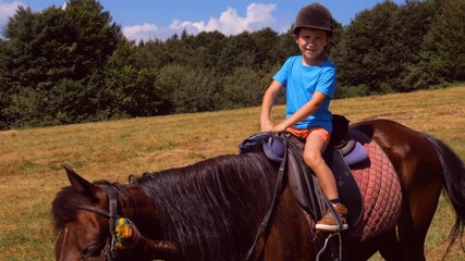 Happy boy in helmet riding brown horse in mountains