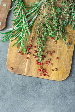 Fresh Provence Herbs Rosemary Thyme Twigs red Pink Peppers on Aged Wood Cutting Board Knife on Dark Concrete Stone Table. Top View. Mediterranean Cuisine Meat Fish Seasoning Ingredients. Copy Space