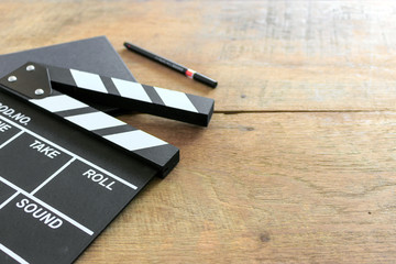film director's desk. clapboard, book and pen on wood table with soft-focus and over light in the background. top view shot