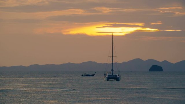 Catamaran in the roadstead and a long-tail boats floating in the sea at sunset