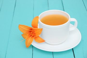 White cup of green tea on turquoise boards with bud on hemerocallis saucer