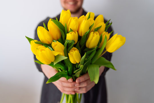 man holds bouquet of yellow tulips in front of him. romantic gift for woman. white background