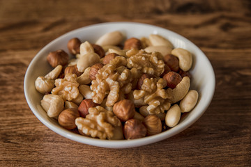 nuts, in a white bowl, fried on a dark wood background, mixture of walnuts, almonds and roasted nuts, top view