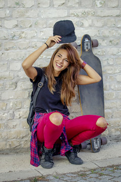 Young skate board girl relax in front of brick wall and smile