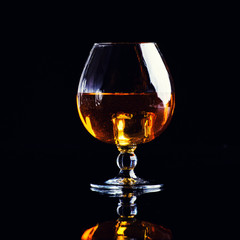 glass with cognac with splash on a black background
