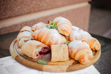 Fresh croissants with crispy crust with cherry and chocolate filling are decorated with sugar powder and mint leaves. Closeup.