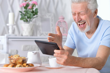senior man using tablet while drinking tea 