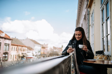 Fototapeta premium Enjoying cup of coffee and using phone on the balcony at old city core.