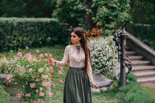A girl is walking in a blooming garden, with a vintage blouse and a long skirt, chestnut long hair. she gently cares for her flowers. Sweetheart gardener. Artistic Photography