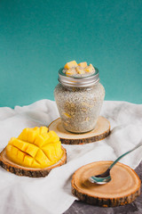 Chia pudding with yellow mango pieces on white linen cloth on turquoise background. Vegan healthy diet concept.