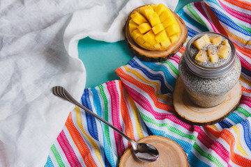 Chia pudding with yellow mango pieces on background of clorful striped kitchen cloth. Vegan healthy diet concept.