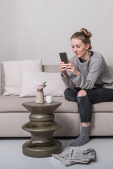 Eine Frau sitzt zuhause auf dem Sofa und sieht sich etwas auf ihrem Telefon an