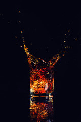 Isolated shot of whiskey with splash on black background, brandy in a glass