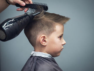 Side view of cute boy getting hairstyle by hairdresser in barbershop. - 196392619
