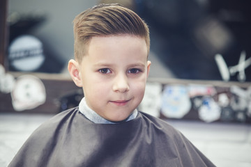 Barber shop. Boy with a totally new look is looking to a camera.