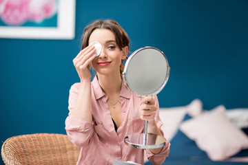 Young woman removing makeup with a cotton swab sitting in the blue bedroom