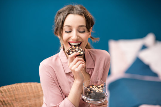 Beautiful woman enjoying a chocolate sitting on the blue wall background indoors