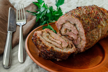 on a clay plate lies a cut meatloaf with a juicy middle, beside a brown linen napkin, crumpled light linen tablecloth, fork, spoon, parsley