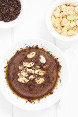 Chocolate pudding or flan dessert with caramel sauce, roasted almond slices and chocolate shavings, photographed overhead with natural light (Selective Focus, Focus on the top of the dessert)