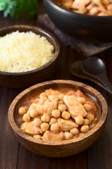 Chicken and chickpea stew or tagine in wooden bowl with couscous in the back, photographed with natural light (Selective Focus, Focus one third into the image)