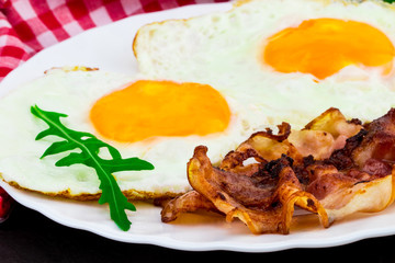 Breakfast with fried eggs, bacon and rucola salad on dark stone background