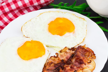 Breakfast with fried eggs, bacon and rucola salad on dark stone background