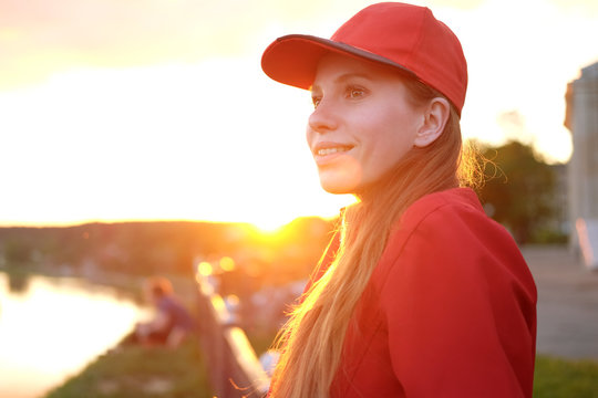 young redhead woman in red cap and jacket urban portrait in sunset light