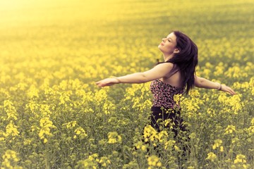 Naklejka na ściany i meble Beautiful woman in meadow of yellow twist from behind. Attractive authentic young girl enjoying the luxury of warm summer sun sunshine and wellbeing youth in wide landscape. Part of series