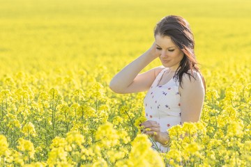Fototapeta premium Beatiful youth woman with flower in summer meadow looking down. Beautiful girl eyes closed in yellow flowers field infinite horizon. Sunny sun sunshine and authentic lifestyle in windy weather hair