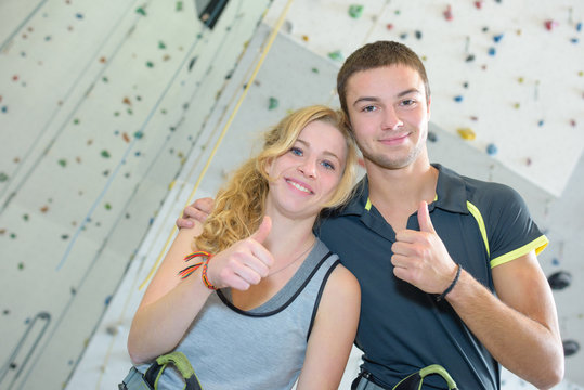 Young couple giving thumbs up in front of climbing wall