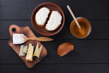 Hard cheese on a wooden board, sandwiches with soft cheese, honey in glass dishes, copy space, minimalism, cheese pattern, wooden dark background, healthy food, wooden cutlery