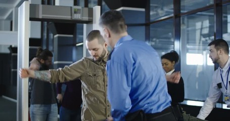 Man in guard uniform conducting checking control with metal detector working with passenger in airport.