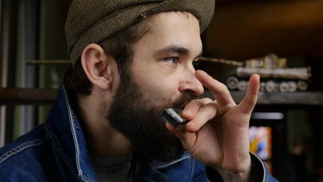 Musician plays the harmonica. Young men enjoying music by harmonica. Close-up portrait of expressive young man playing harmonica.