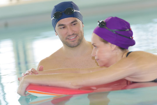 man helping woman in swimming pool with float
