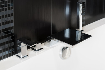 Basin mixer tap, bath shower mixer, waterfall faucet and shower head on the side of the bathtub close-up. rectangular modern design in black and white.