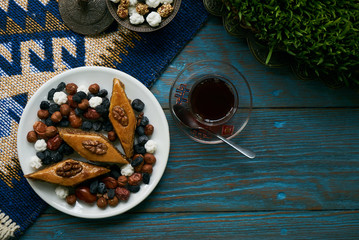 Azerbaijan national pastry pakhlava with sweet snack and glass of traditional black tea on wooden table with green semeni wheat grass background , Novruz tray spring celebration