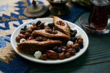 Azerbaijan national pastry pakhlava with sweet snack and glass of traditional black tea on wooden table with green semeni wheat grass background , Novruz tray spring celebration