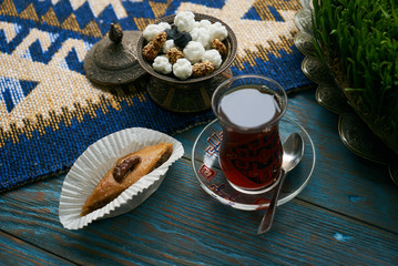 Pakhlava or baklava with nuts and honey. Novruz tray with Azerbaijan national pastry and drinking glass of black tea on blue rustic wooden table background, top view. Delicious dessert holiday food