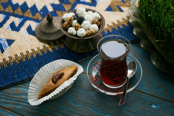 Pakhlava or baklava with nuts and honey. Novruz tray with Azerbaijan national pastry and drinking glass of black tea on blue rustic wooden table background, top view. Delicious dessert holiday food